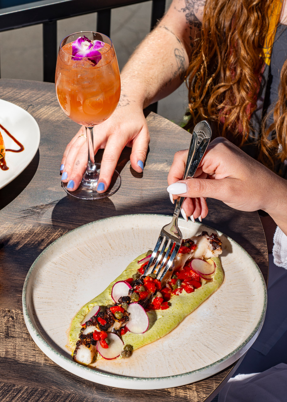 Guest cutting into a plated seafood dish with colorful garnish.