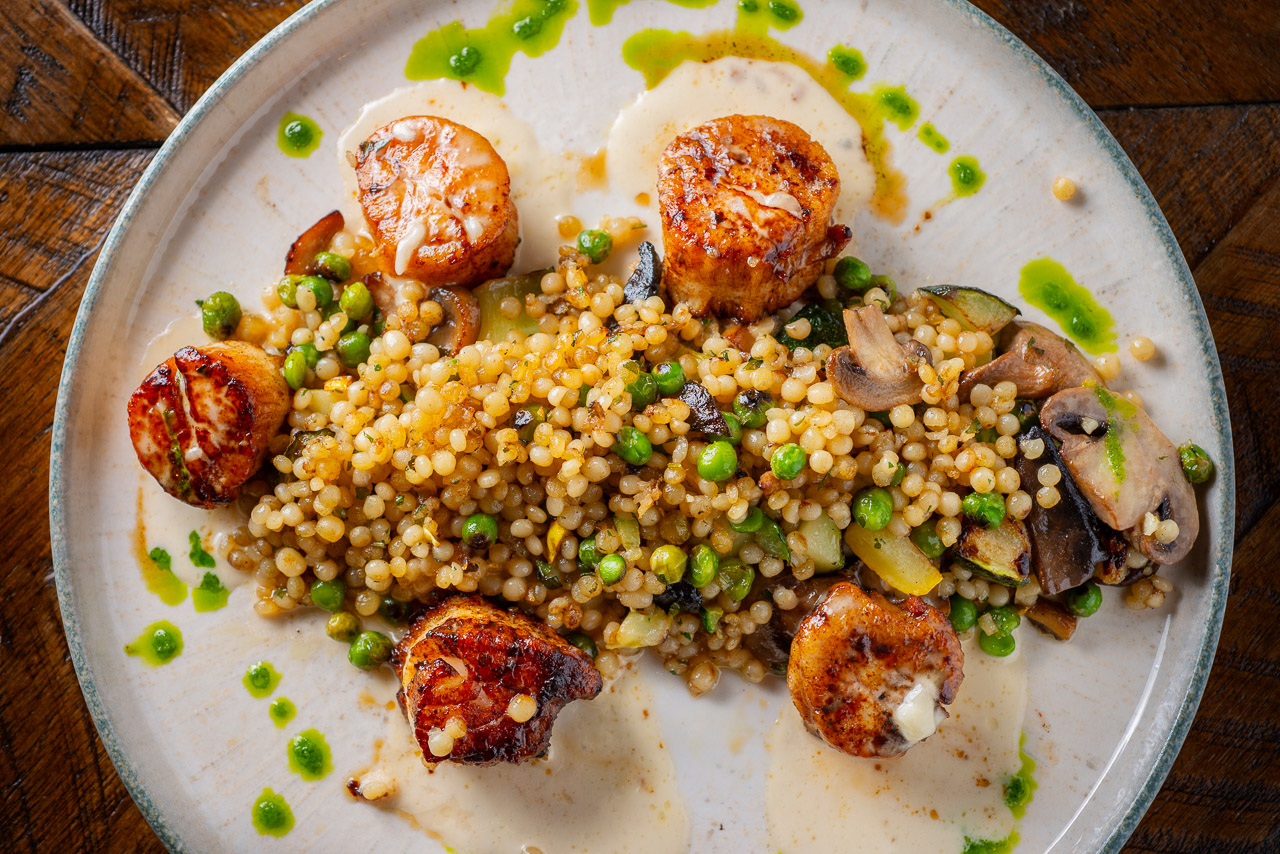 Shadows-on-the-Hudson-Summer2026-specials-entrees-2 Seared scallops served over pearl couscous with peas and vegetables.